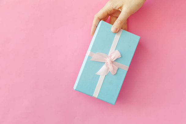 Simply design female woman hand holding blue gift box isolated on pink pastel colorful trendy background - Photo, Image