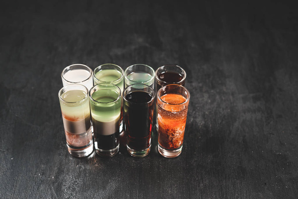 Set de cócteles alcohólicos en vasos de chupito (shooters) sobre fondo de madera negro
 - Foto, imagen