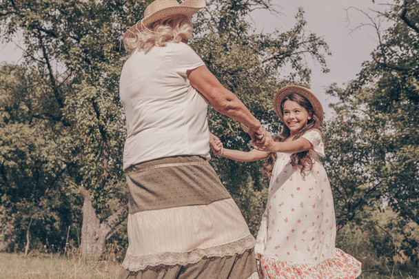 Щаслива бабуся танцює зі своєю онукою в парку. Літня жінка грає з дитиною на тлі дерев. Щасливий старість
. - Фото, зображення