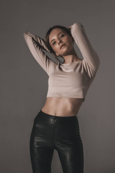 Attractive sexy fashion woman with brunette hairstyle in reglan and leather pants. Portrait of seductive hot stylish woman model on white background in studio - Φωτογραφία, εικόνα