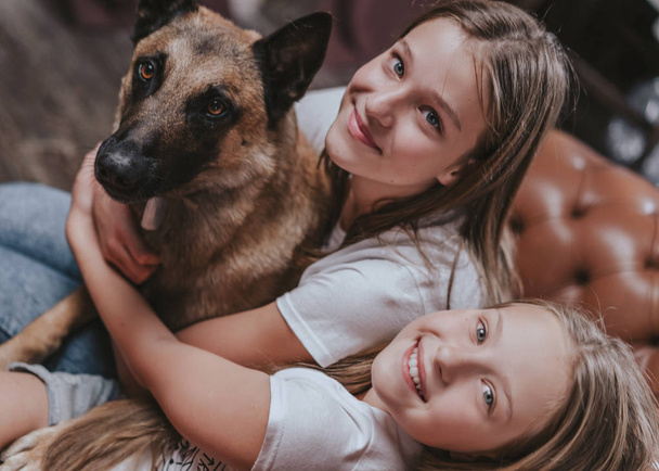 ベッドで自宅で犬と遊んでいる2人の若いかわいい女の子の肖像画。ペットケアの概念。幸せな瞬間 - 写真・画像