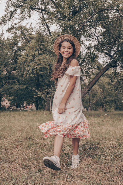 Krásný portrét mladé dívky s krásnou tváří. Oblečený v kostýmech a klobouku. Sluneční den v létě. Hezký úsměv, dítě. Šťastný mladý věk - Fotografie, Obrázek