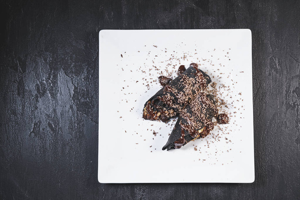 Deliciosas panquecas frescas com chocolate e bananas, canela em uma placa branca em um fundo de mesa de pedra preta
 - Foto, Imagem