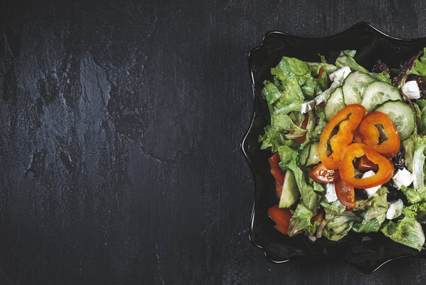 köstlicher frischer Salat mit Gemüse und Feta-Käse. griechischer Salat in einem schwarzen Teller auf schwarzem Steintischhintergrund - Foto, Bild