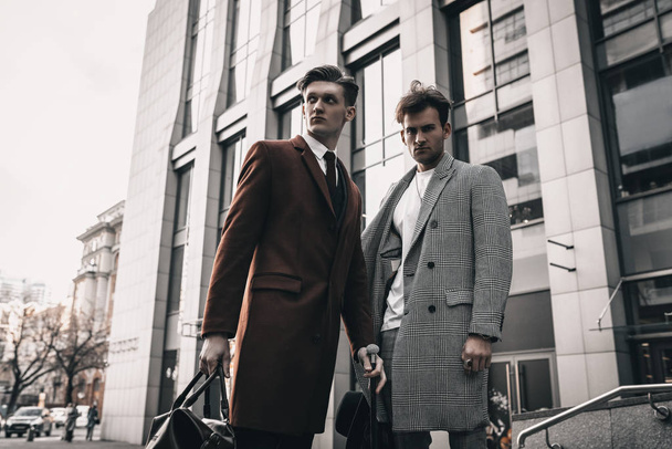 Jovens dois homens modelos andando na rua da cidade em roupas clássicas e casuais com penteado elegante. Homem barbudo retrato da moda
 - Foto, Imagem
