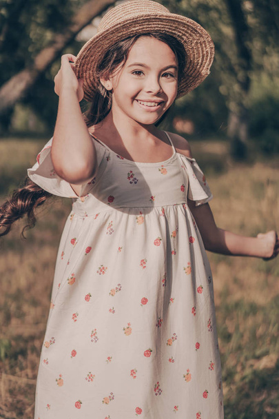 Portrait of beautiful young happy girl in hat and sundress in park. Happiness lifestyle. Cute caucasian pretty child model in sunset in garden - Foto, Bild