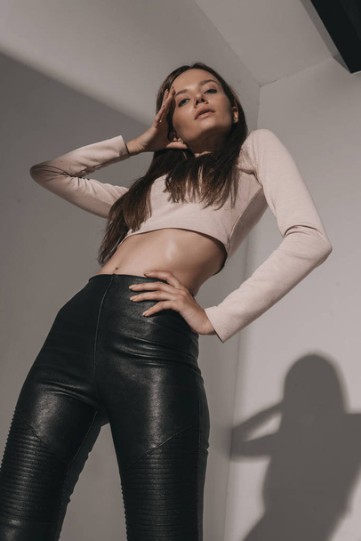Attractive sexy fashion woman with brunette hairstyle in reglan and leather pants. Portrait of seductive hot stylish woman model on white background in studio - 写真・画像