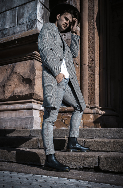Модный портрет молодого человека на сером пальто, черной шляпе и белом свитере, гуляющего по улицам города. Модель стрельбы
 - Фото, изображение