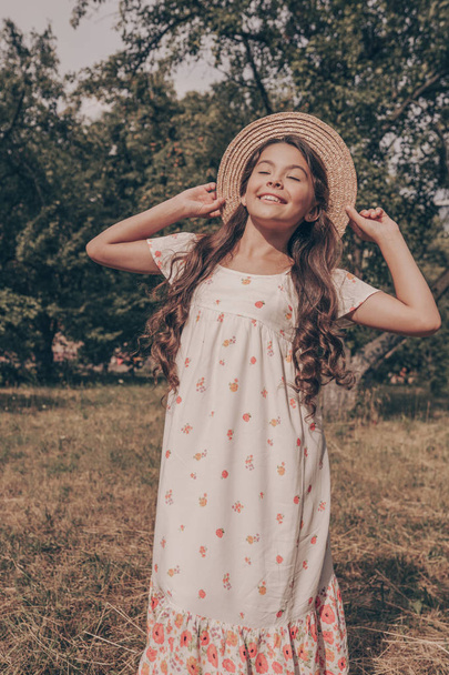 Nuori kaunis onnellinen tyttö auringonmekko ja hattu pelata osittain. Kaunis tytär kesävaatteissa luonnon taustalla. Hymyile lapsi kauneus muotokuva
 - Valokuva, kuva