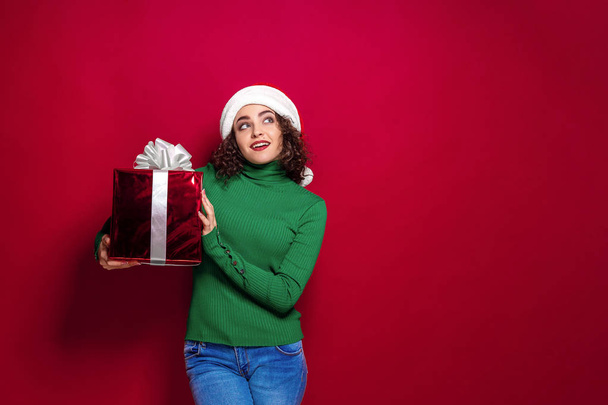 Beautiful fashion woman in santa claus hat. Warm Christmas sweater holding gift box on. - Valokuva, kuva