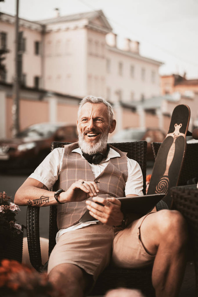 Lächelndes Männerporträt auf der Straße der Stadt. erwachsener bärtiger Mann in Freizeitkleidung, der freiberuflich arbeitet. zufriedene Geschäftsleute machen sich Notizen in Notizbuch oder Laptop. Geschäftskonzept - Foto, Bild