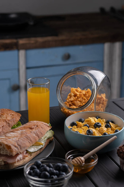 Завтрак. Утренняя еда. Домашняя еда. Кухня. Свежий сэндвич, багет, кукурузные хлопья с медом и ягодами. Черный стол
 - Фото, изображение