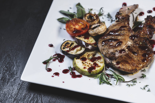 Lahodné čerstvé maso a zelenina vařené na grilu v bílém talíři na černém kamenném stole na pozadí - Fotografie, Obrázek