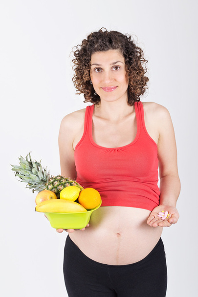 Pregnant woman holding fresh fruits and pills - Foto, Imagen