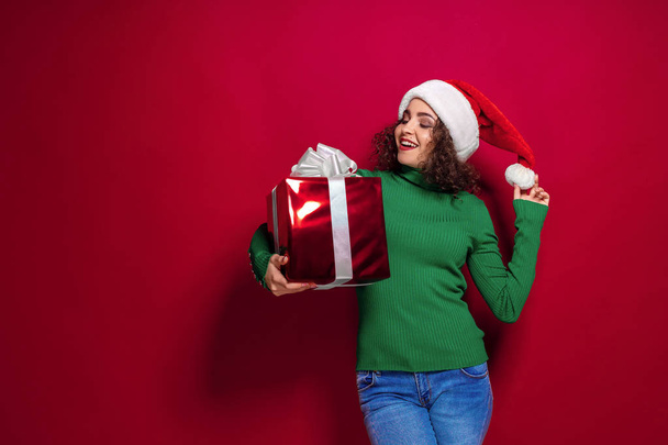 Beautiful fashion woman in santa claus hat. Warm Christmas sweater holding gift box on. - Foto, imagen