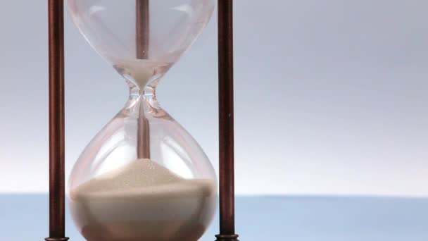 Closeup of a sand clock on the left side with space on the right side. Closeup of a glass sand clock on white with golden balls instead of sand falling. Time - Footage, Video