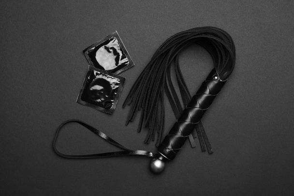 Whip and condoms on black background, top view. Sex game - Photo, image