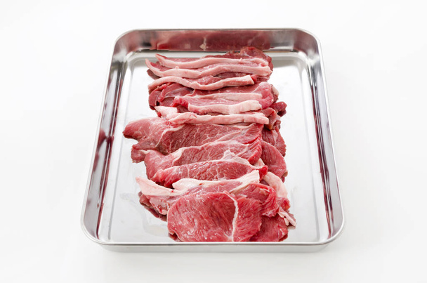 Carne di agnello cruda su un vassoio in acciaio inox su sfondo bianco
. - Foto, immagini