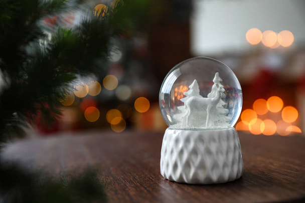 Snow globe on wooden table against blurred background, space for text. Bokeh effect - Фото, зображення
