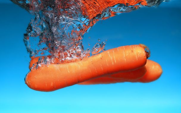Carrot in the water splash over blue - 写真・画像