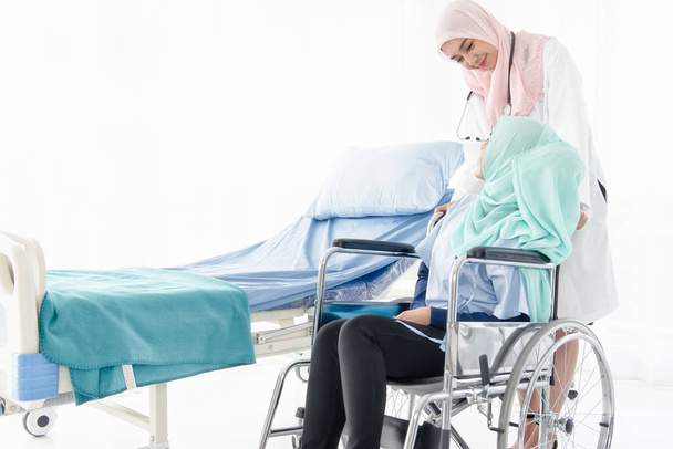 Moslim arts die de patiënt in een rolstoel draagt. - Foto, afbeelding