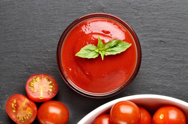 Primer plano de ketchup casero hecho de tomates cherry frescos, ajo, albahaca en plato de pizarra negra. Vista superior
. - Foto, imagen