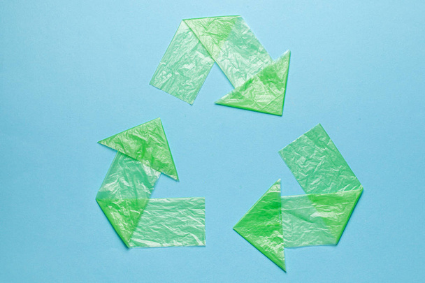 Mavi arka plandaki yeşil poşetlerdeki geri dönüşüm plastiğini imzala. Tek kullanımlık torbalar ve geri dönüşümle çevre kirliliği - Fotoğraf, Görsel