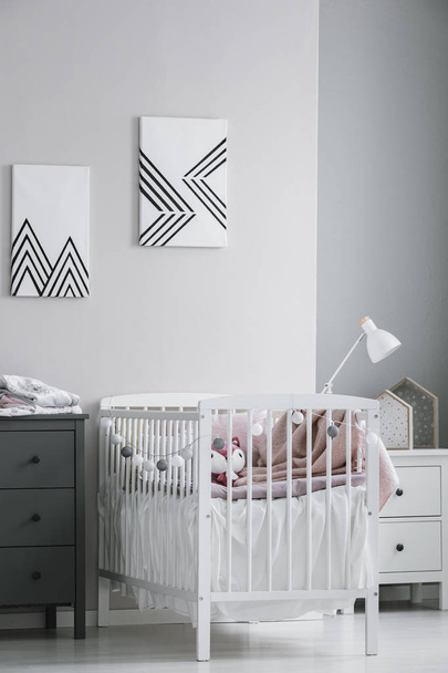 White crib with paste pink bedding and cotton balls in bright bedroom interior - Foto, imagen