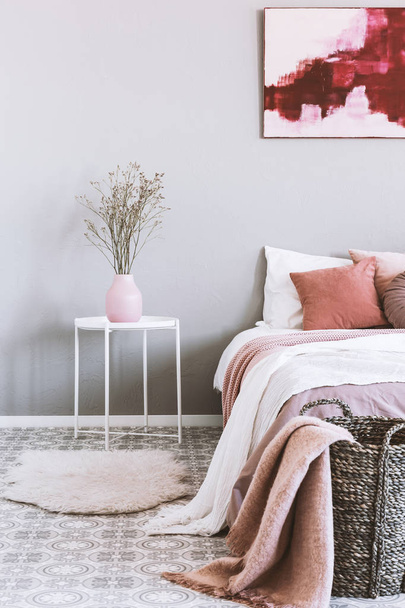 Vertical view of pink and grey bedroom interior with wicker basket and flowers in vase - Foto, Bild