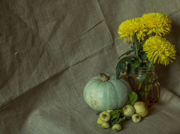Yellow chrysanthemums in a glass mug, a white pumpkin and small wild apples on a rough fabric , autumn still life - Valokuva, kuva