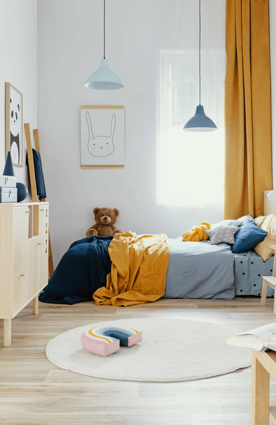 Teddy bear on single wooden bed in blue and orange bedroom interior - Foto, afbeelding