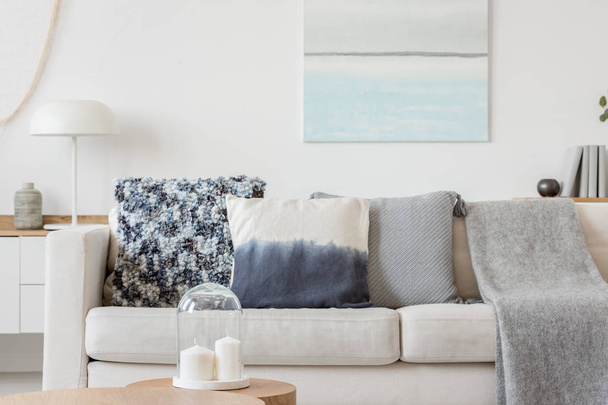 Abstract paste blue and white painting on empty white wall behind beige couch with pillows - Foto, imagen