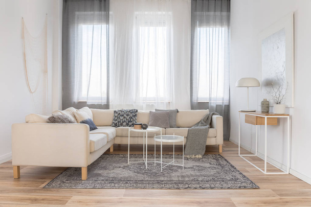 Tavolini industriali bianchi in luminoso soggiorno interno con grande divano ad angolo
 - Foto, immagini
