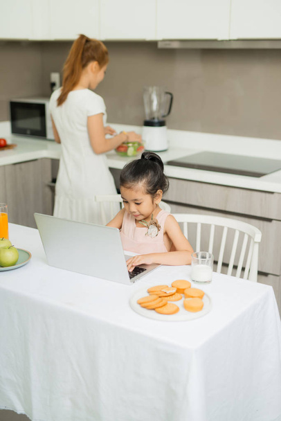 Szczęśliwa azjatycka rodzina je śniadanie i widzi cyfrową tabletkę w kuchni w domu. Zdrowe jedzenie i poranne zajęcia - Zdjęcie, obraz
