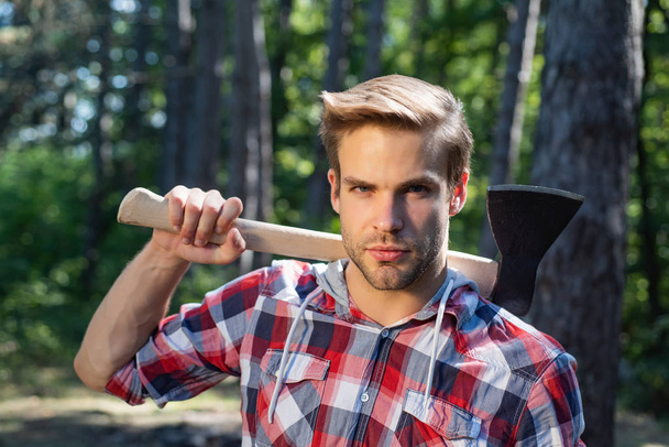 Lumberjack on serious face carries axe on shoulder. - Foto, Imagen