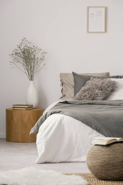 Wooden nightstand table next to king size bed with white and grey bedding in simple bedroom interior - Photo, Image
