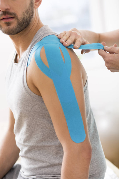 Physiotherapist covering selected fragments of young man's body with special structure patches during kinesiotaping therapy - Foto, immagini