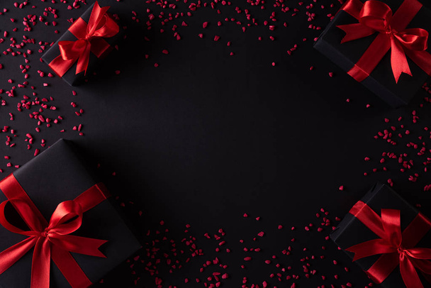 Top view of black christmas boxes with red ribbon on black background with copy space for text. black Friday composition. - Photo, Image