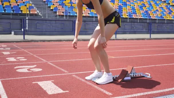 Szczupła młoda dziewczyna sportowiec w pozycji, aby rozpocząć bieg na stadionie - Materiał filmowy, wideo