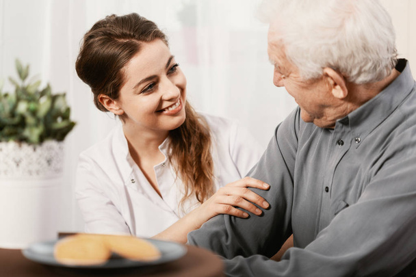 Smiling young nurse sitting at table with senior patient - Photo, Image