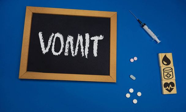 tablet de madeira na mesa médica azul com a palavra VOMIT
 - Foto, Imagem