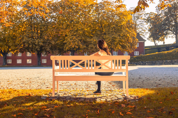 Красива самотня дівчина сидить на білій лавці восени
  - Фото, зображення