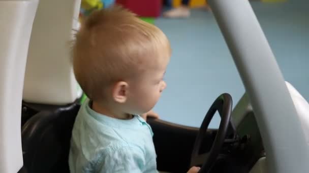 Boy sitting in a toy car. Baby closes car door and drives. Child in children’s play center. - Footage, Video