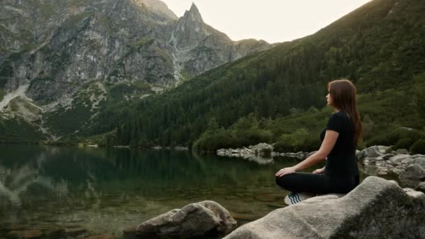 Mujer sana medita en un lago de montaña, practicando yoga, disfruta de la tranquilidad alta en las montañas
 - Metraje, vídeo