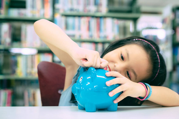 Asian Girl ręka trzyma Piggy i wkłada monetę do skarbonki na przyszłe życie. Koncepcja inwestycji i oszczędności. - Zdjęcie, obraz