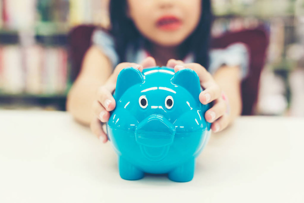 Cose się ręka dziewczyna trzyma Piggy i wkładając monetę do skarbonki do przyszłego życia. Koncepcja inwestycji i oszczędności. - Zdjęcie, obraz