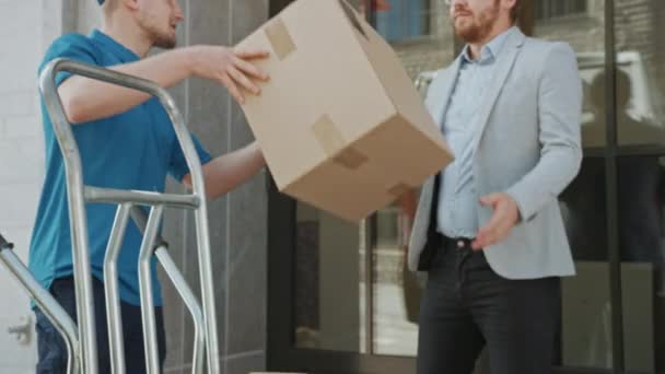 Delivery Man Gives Postal Package to a Business Customer, Who Signs Electronic Signature POD Device. In Stylish Modern Urban Office Area Courier Delivers Cardboard Box Parcel to a Man - Filmagem, Vídeo
