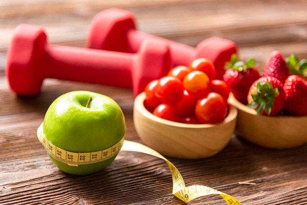 Здоровый образ жизни для женщин диета со свежими фруктами салат и гантели спортивное оборудование измерения ленты, фрукты здоровые зеленые яблоки на деревянном. Здоровая концепция. выбрать фокус
 - Фото, изображение