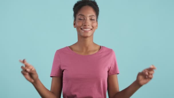 Досить усміхнена афро-американська дівчина радісно схрестила пальці з надією зробити бажання на камеру на синьому фоні
 - Кадри, відео
