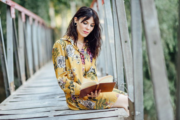Young woman reading a book on a rural bridge. - Fotoğraf, Görsel